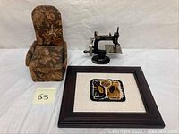 The full lot showing the upholstered doll armchair with floral fabric, the framed needlework cats textile, and the antique child-sized Singer sewing machine.