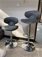 Two black upholstered bar stools with curved backs and round chrome bases, shown at an angle to display the overall style and condition.