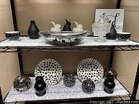 Black and white decorative ceramics, glass items on metal shelves. Showcases polka dot bowls, cut glass dish, vases, wood candle holders and decorative balls.
