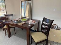 Full view of wood table with two chairs, table set with plates, bowls, and a bowl of green apples providing scale and context.