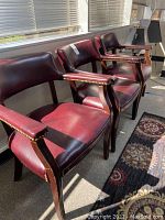 Set of three wood and faux leather chairs with brass brads in sunlit room, showing side profile and overall condition.