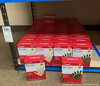 Shelf with 44 boxes of At Home incandescent mini Christmas lights. Boxes are red and white with 100 lights per box. Both clear and green lights are included.