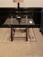 First end table with clear glass top and dark wood X-shaped base, slight scratches visible on glass surface