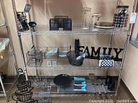 Kitchen shelf with various metal mesh utensil holders, decorative metal art pieces including coffee cup designs, a black 'FAMILY' sign, and metal bowls and baskets.