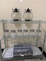 Two round glass and metal lanterns on a wire shelving unit