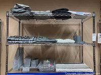 Metal wire shelving unit holding folded linens, fabric bathroom curtains, bathroom accessories, plastic baskets, and office desk organizers arranged on shelves.