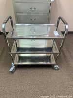Full view of the Winco metal rolling cart with three shelves and four wheels.