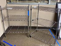 Two chrome-finished metal shelving units side by side against a wall on carpeted floor. One unit leans slightly to the side.