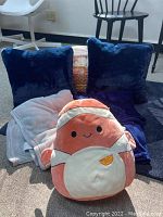 Photo showing two navy blue throw pillows, one cream and one navy blue throw partially visible, and an orange slice plush character in front of the pillows.