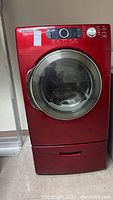 Front view of red Samsung electric dryer with glass door and control panel with dial and buttons on top right.