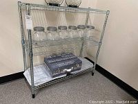 Front view of metal wire shelving unit with six glass storage jars on the second tier and decorative box with cloth on third tier, two glass decorative bowls on top tier.