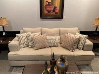 Front view of the beige upholstered sofa showing all seven decorative pillows arranged on the back cushions.