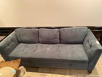 Front view of blue upholstered sofa showing tufted seating area and three back cushions.