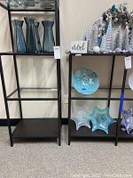 Photo of shelving units displaying four turquoise glass vases, one turquoise decorative bowl, and two star-shaped glass decor pieces on stands.