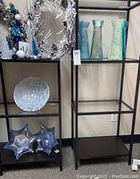 Four glass vases on black shelves, two star-shaped glass bowls on lower shelf, white decorative bowl with sea life designs on middle shelf.