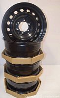 Four black steel rims stacked vertically showing their circular vent holes and bolt pattern