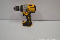 Photo of used DEWALT DCD991B 20V MAX XR brushless cordless drill driver set on white surface showing left side profile of the drill with yellow and black housing.