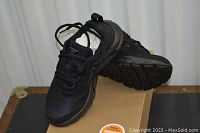 Pair of black kids sneakers shown on top of a cardboard box, shoes facing forward showing shape and design.