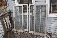 Front view of two leaded glass window panels leaning against siding