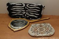 Black and white zebra pattern beaded purse, decorative wooden hand mirror, and floral beaded purse laid on a wooden surface.