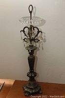 Full view of antique standing ashtray showing ornate bronze metal base, spiral handle, and cut crystal dish with hanging prisms