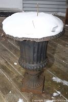 Full view of the planter showing its shape, rust, and snow covering the top.