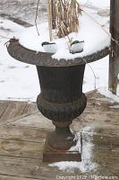 Cast iron urn planter with snow on top showing shape, rim decoration, and pedestal base