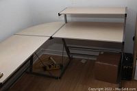 Front-left angled view showing the full L-shaped desk with light wooden desktop and metal frame, placed against white walls and wooden floor.