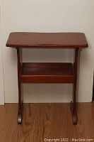 Front view of the red wood end table showing its rectangular shape, top surface, bottom shelf, and gently curved legs.