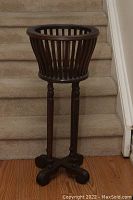 Full view of the wooden fern plant stand showing the round basket top with vertical slats and three tall turned legs.