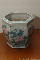 Hexagonal ceramic flower pot seen from the side showing floral patterns with pink roses and green leaves on cream-colored background.