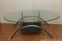 Front view of the oval glass coffee table showing the metal frame and perforated metal shelf below the glass top.