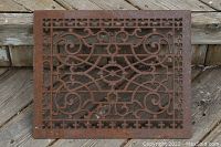 Top view of rusty metal floor grate with decorative scroll and geometric designs placed on a wooden surface.
