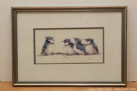 Framed watercolor painting showing four blue jays on a branch, visible signature and title beneath.