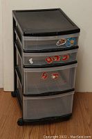 Front view of the 4 drawer plastic shelf showing stickers on drawers and wheels at base.