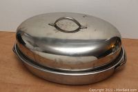 Closed roasting pan with dome lid on a wood surface, showing slight marks on stainless steel.