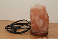 Salt stone lamp unplugged on wooden base displaying natural pink-orange salt stone with attached electrical cord.
