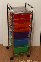 View of metal frame storage shelf with 7 colorful plastic drawers and mesh metal top surface on caster wheels.