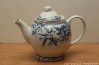Blue and white ceramic teapot front angle showing lid, spout, handle, and detailed floral and bird pattern.