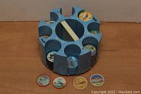 View of blue spinner carousel placed on a wooden surface with stacks of colorful Jello airplane coins inside the slots and four individual coins arranged in front showing airplane illustrations.