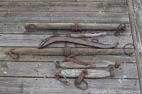 Top view of six wooden wipple trees and metal hardware on wooden floor, showing various shapes and rusted metal fittings.
