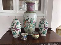 Full front view of all five ceramic items arranged on a table, showing the large central vase, two covered jars, and two small planters.