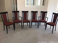 Front view of six wooden dining chairs with red upholstery arranged side by side on a carpeted floor