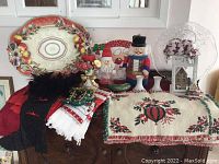 Overall view of Christmas lot items arranged on wooden furniture including Fitz and Floyd tray, textile pieces, nutcracker, Santa decoration and glass plate.