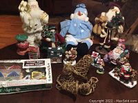 Full view of Christmas decorations including three large Santa figures, blue snowman plush, miniature village pieces, wicker reindeer, and additional small figurines
