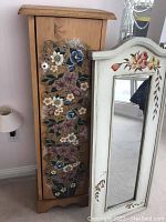 Wooden cabinet next to the standing mirror, showing floral artwork on the cabinet side and the painted details on the mirror frame.