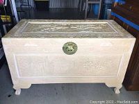 Front view of a carved wooden chest painted white with floral and bird designs and short carved feet.