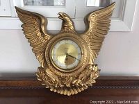 Front view of the gold eagle wall clock with the clock face and eagle wings spread.