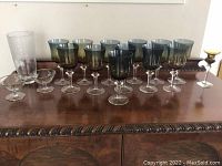 Photo showing entire lot of glassware with large etched vase, 11 colored stemmed glasses, etched dishes and small glass items on wood surface.