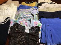 Top view of folded skirts, pants, and blouses showing varied colors and patterns including black, blue, floral, and beige.